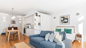 Una sala de estar moderna con un sofá azul, una mesa de comedor de madera y una zona de cocina con armarios blancos.