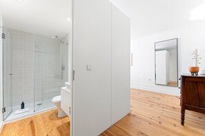 A modern bathroom with a glass shower enclosure, a white toilet, and a wooden floor. - GuestReady - Charming studio in Porto's heart (Porto)