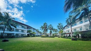 Une cour d’hôtel avec une pelouse, des palmiers et des immeubles à plusieurs étages dotés de balcons.