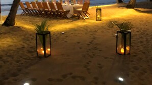 Un espace de restauration aménagé sur la plage, avec des tables et des chaises, des guirlandes lumineuses et des lanternes.