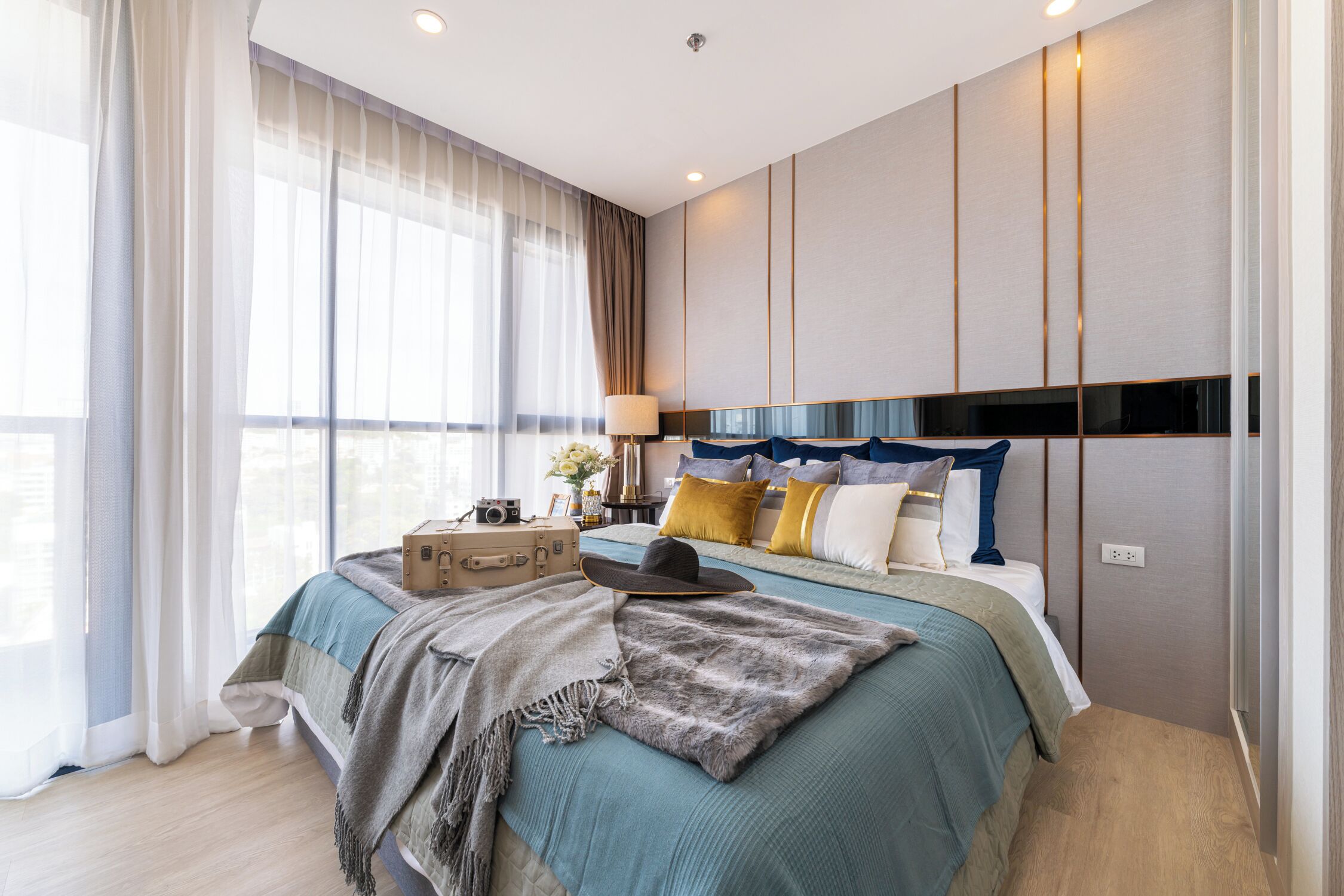 A modern hotel room with a large bed, a suitcase, and a hat on the bed.