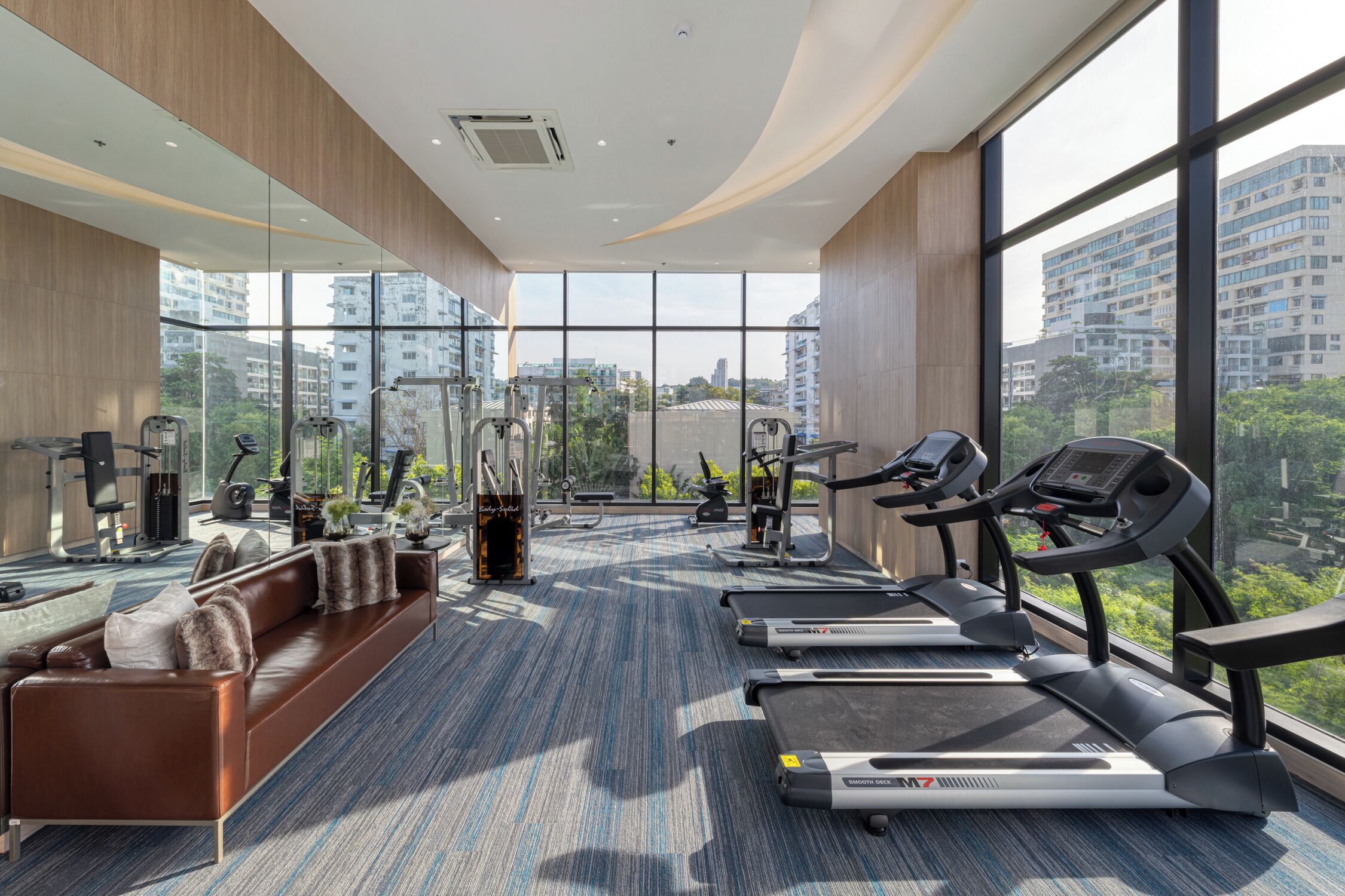 A modern gym with exercise equipment, a sofa, and large windows offering city views.