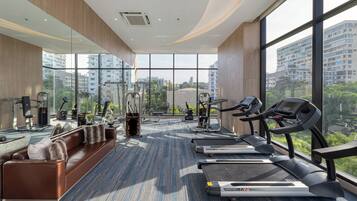 A modern gym with exercise equipment, a sofa, and large windows offering city views.