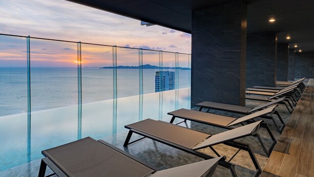 A modern indoor pool area with glass walls, lounge chairs, and a view of the sea. - The Panora Pattaya by PH (Pattaya)
