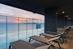 A modern indoor pool area with glass walls, lounge chairs, and a view of the sea. - The Panora Pattaya by PH (Pattaya)