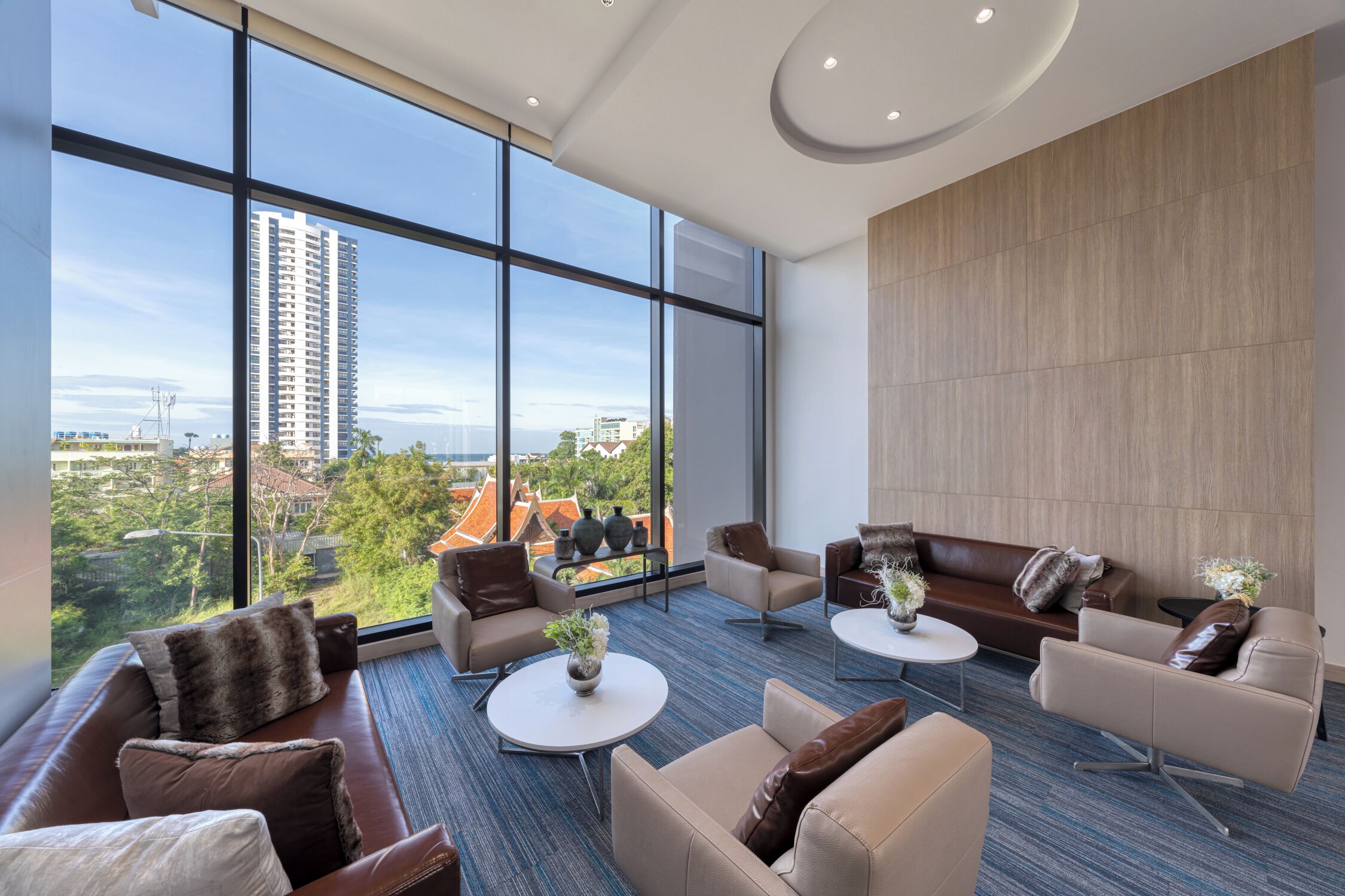 A spacious living area with a large window, a brown leather sofa, a white coffee table, and a brown leather couch.
