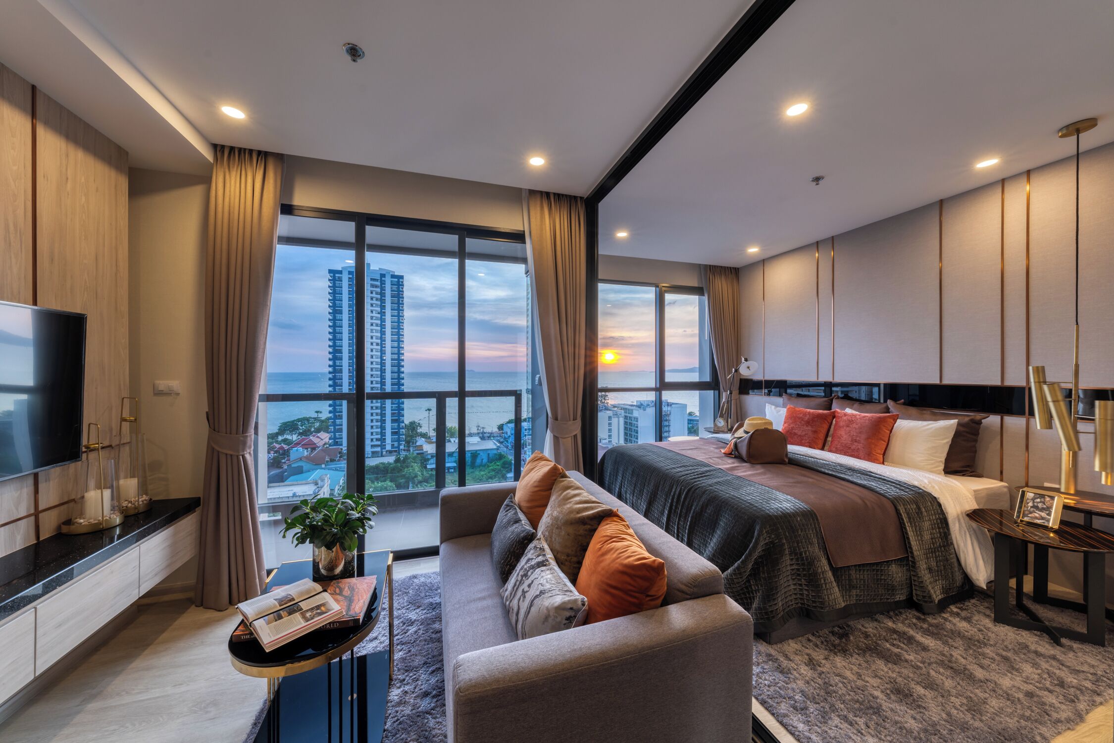 A modern hotel room with a large bed, a sofa, a TV, and a view of the cityscape.
