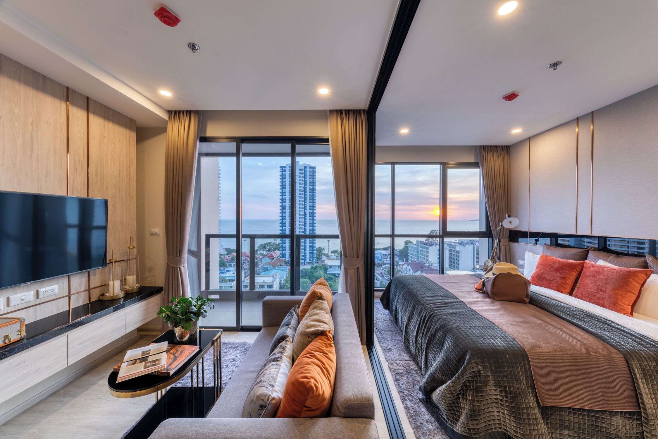 Een moderne hotelkamer met een grote televisie, een bank, een bed en uitzicht op de stad.