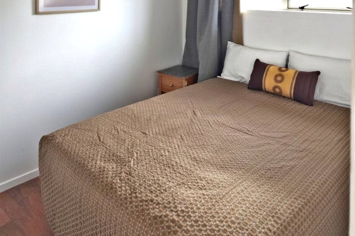 A bedroom with a bed, a nightstand, a window with curtains, and a wall-mounted light fixture.