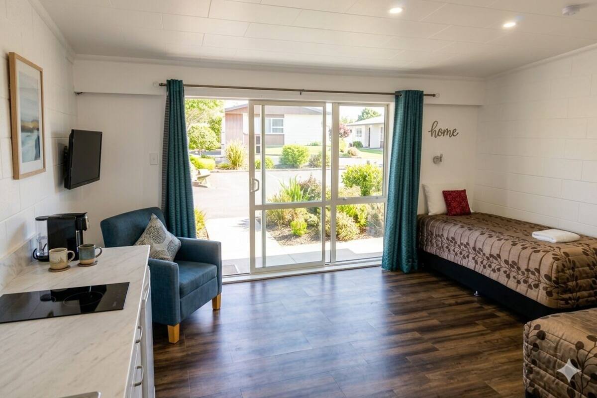 A room with a bed, a desk, a chair, a TV, and a sliding glass door to the outside.