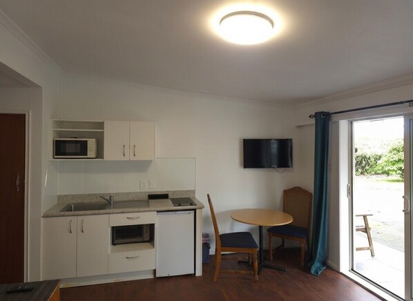 A compact kitchen with a microwave, oven, and sink, a dining area with a table and chairs, and a TV mounted on the wall.