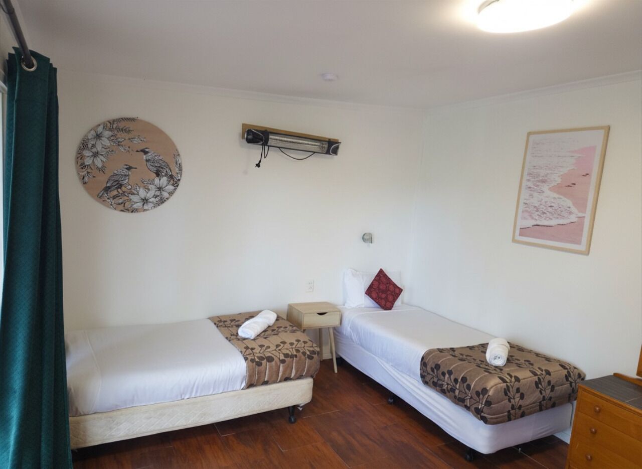 A room with two beds, a small table, a wall-mounted heater, and a map on the wall.