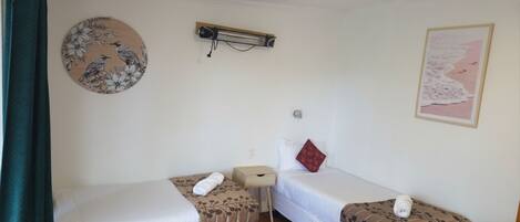 A room with two beds, a small table, a wall-mounted heater, and a map on the wall.