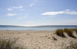 A beach with sand, grass, and a clear sky.