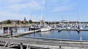 Ein Yachthafen mit mehreren vertäuten Booten, Holzstegen und einem entfernten Gebäude mit einem Turm.