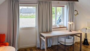 Una habitación con un escritorio de madera, una silla, una lámpara y vistas a un edificio.