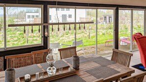 Un comedor con una mesa dispuesta para dos, ventanas amplias y vistas a un jardín y edificios.