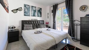 Une chambre à coucher comprenant un lit, une table de chevet, une commode, une fenêtre avec des rideaux et des œuvres d’art accrochées aux murs.