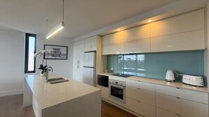 A modern kitchen with a central island, built-in appliances, and a view through the window. - Modern coastal stay in the heart of Scarborough (Scarborough)