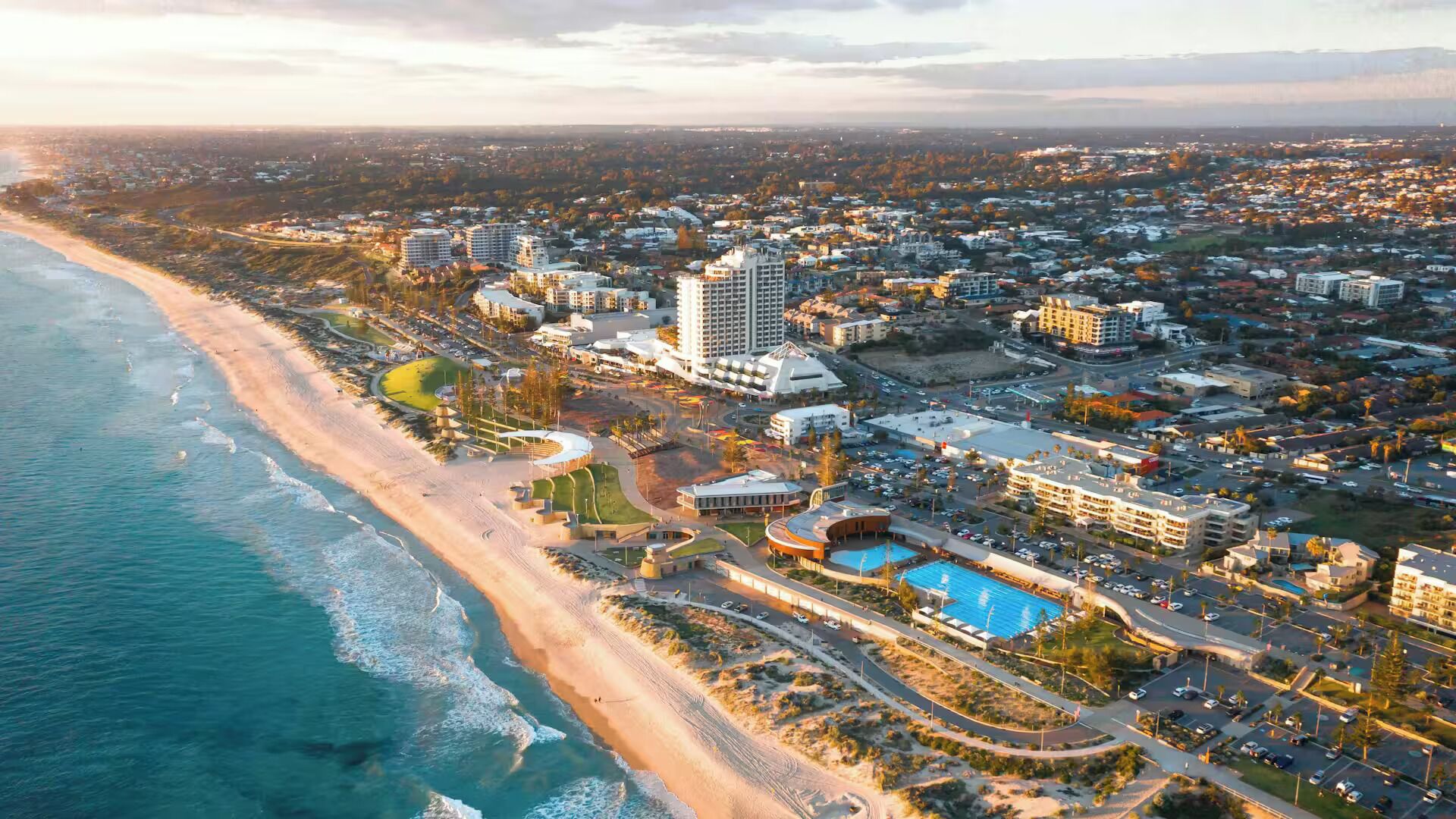 Luchtbeeld van een kustplaats met een strandhotel, inclusief een zwembad en een parkeerplaats.