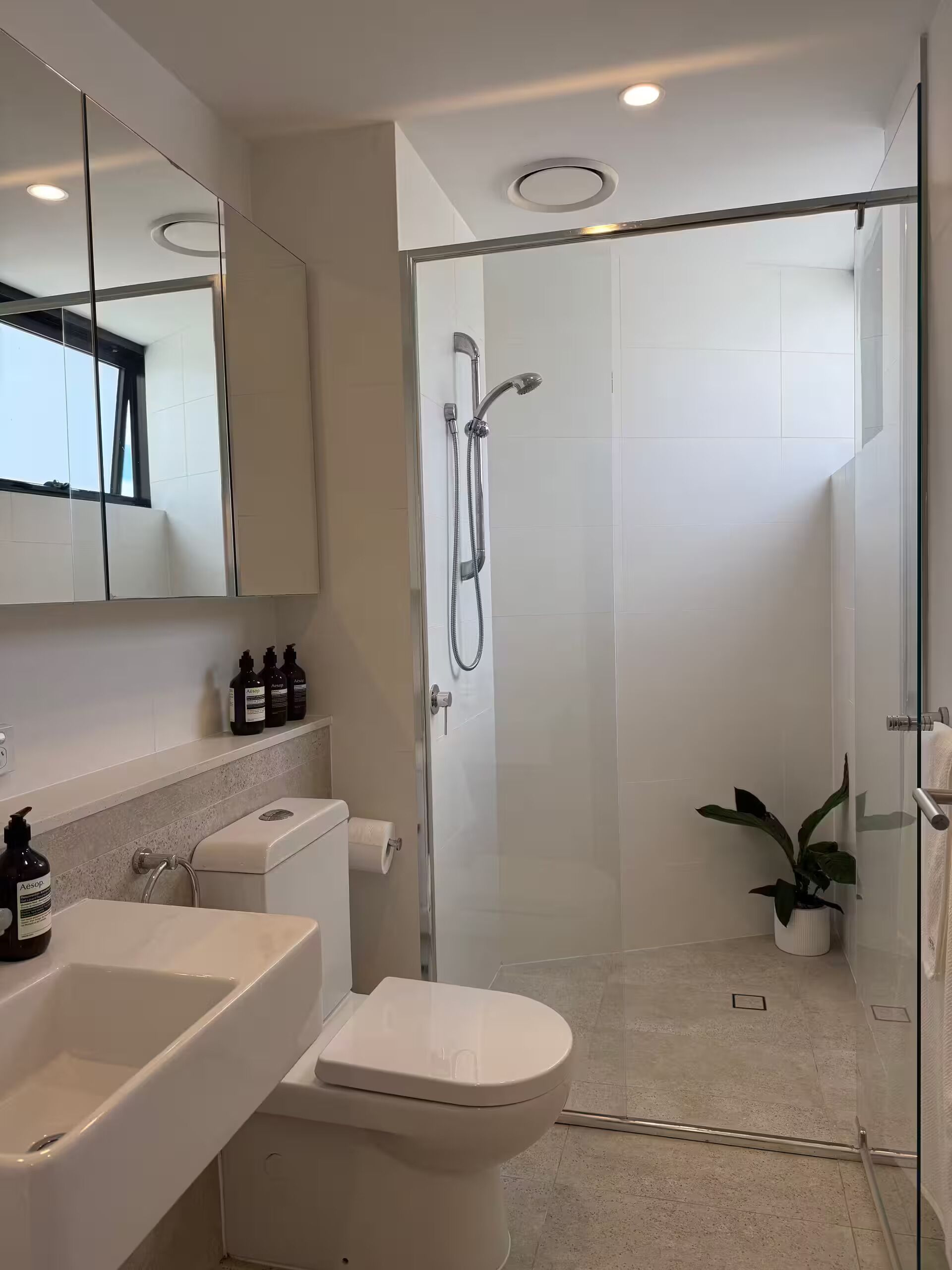 Een moderne badkamer met een douchecabine van glas, een toilet, een wastafel en een spiegel.