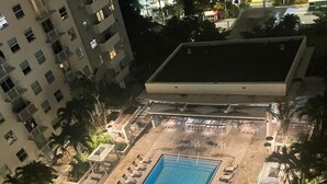 An aerial view of a hotel with a rectangular swimming pool surrounded by lounge chairs and umbrellas, with palm trees and a multi-story building in the background. - Luxury Prime Brickell Condo, Pool, Gym, Free Parking (Miami)