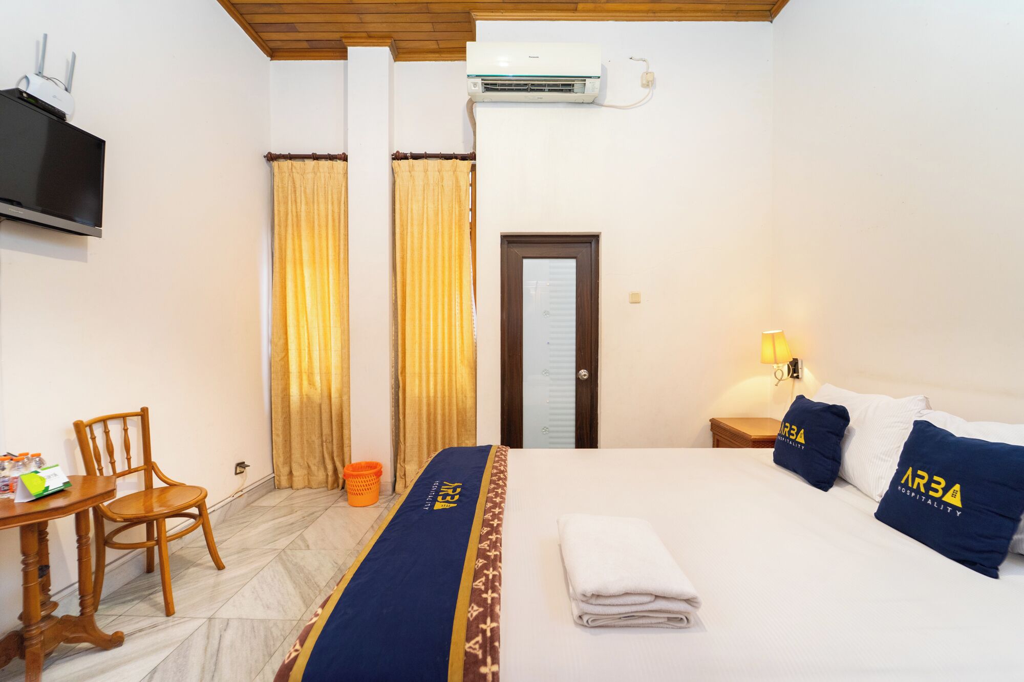 Une chambre d’hôtel équipée d’un lit, d’une télévision, d’un climatiseur, d’un bureau avec une chaise et de rideaux.