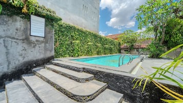 A swimming pool with steps leading to it, surrounded by greenery and a building with a wall covered in plants.