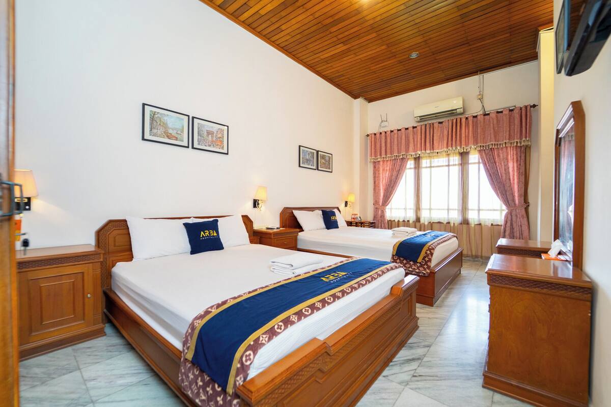 A hotel room with two beds, wooden headboards, a marble floor, a wooden ceiling, and a window with pink curtains.