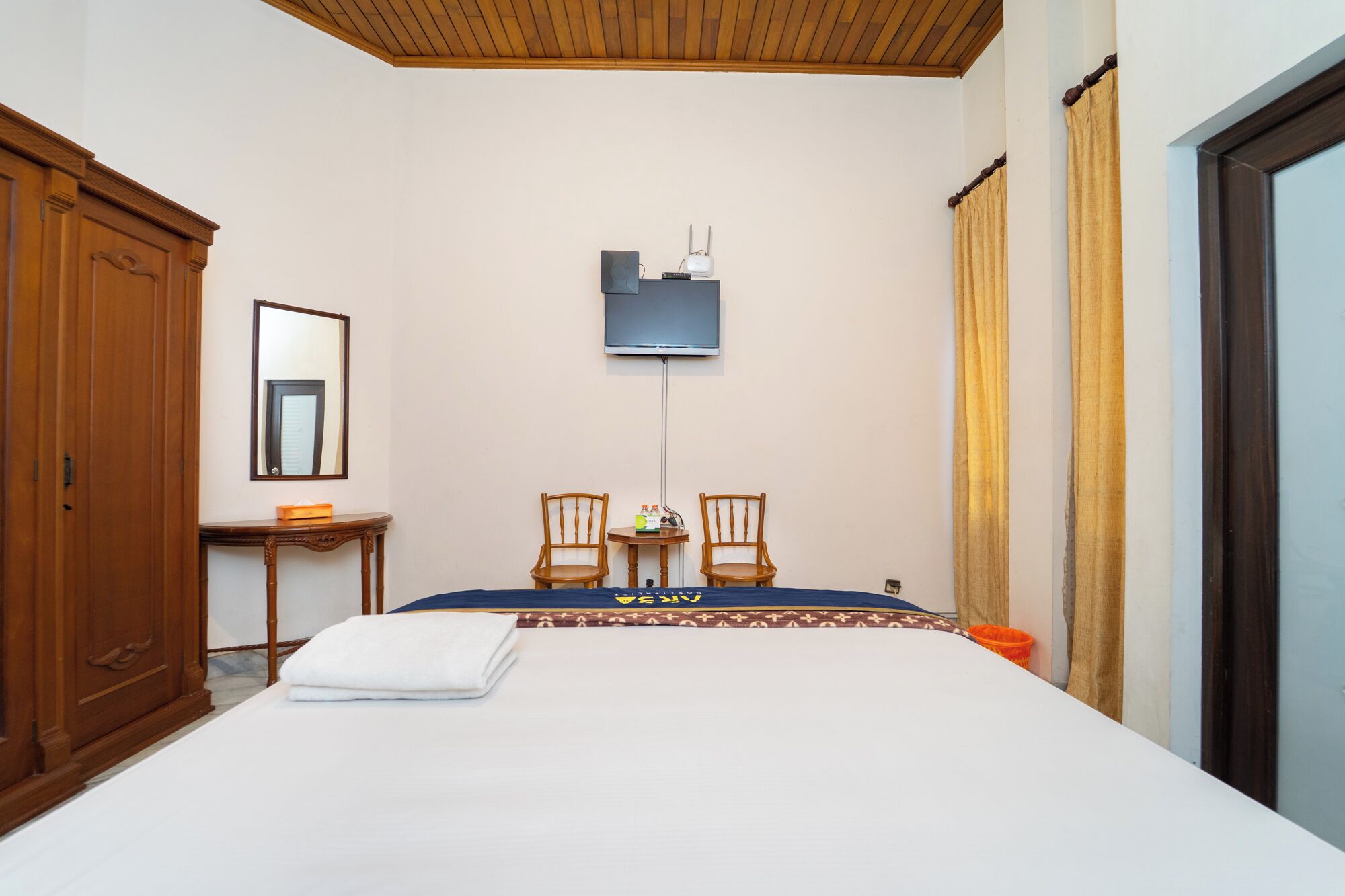 A hotel room with a bed, two chairs, a small table, a mirror, and a television.