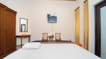 A hotel room with a bed, two chairs, a small table, a mirror, and a television.