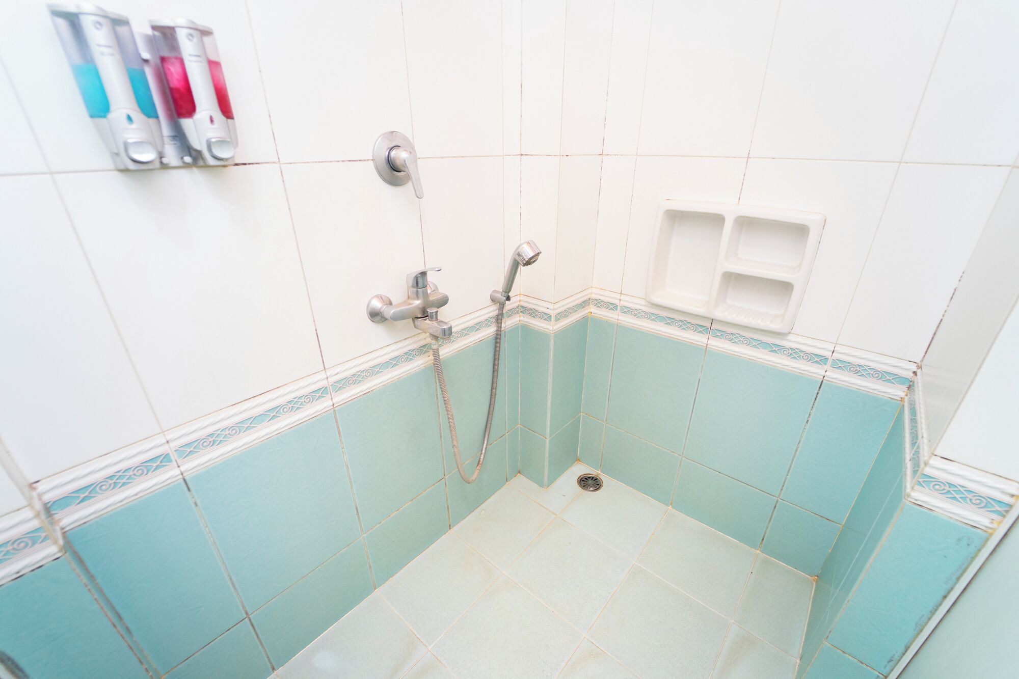 Une salle de bain avec des carreaux blancs et turquoise, une douche et un distributeur de savon à mains fixé au mur.