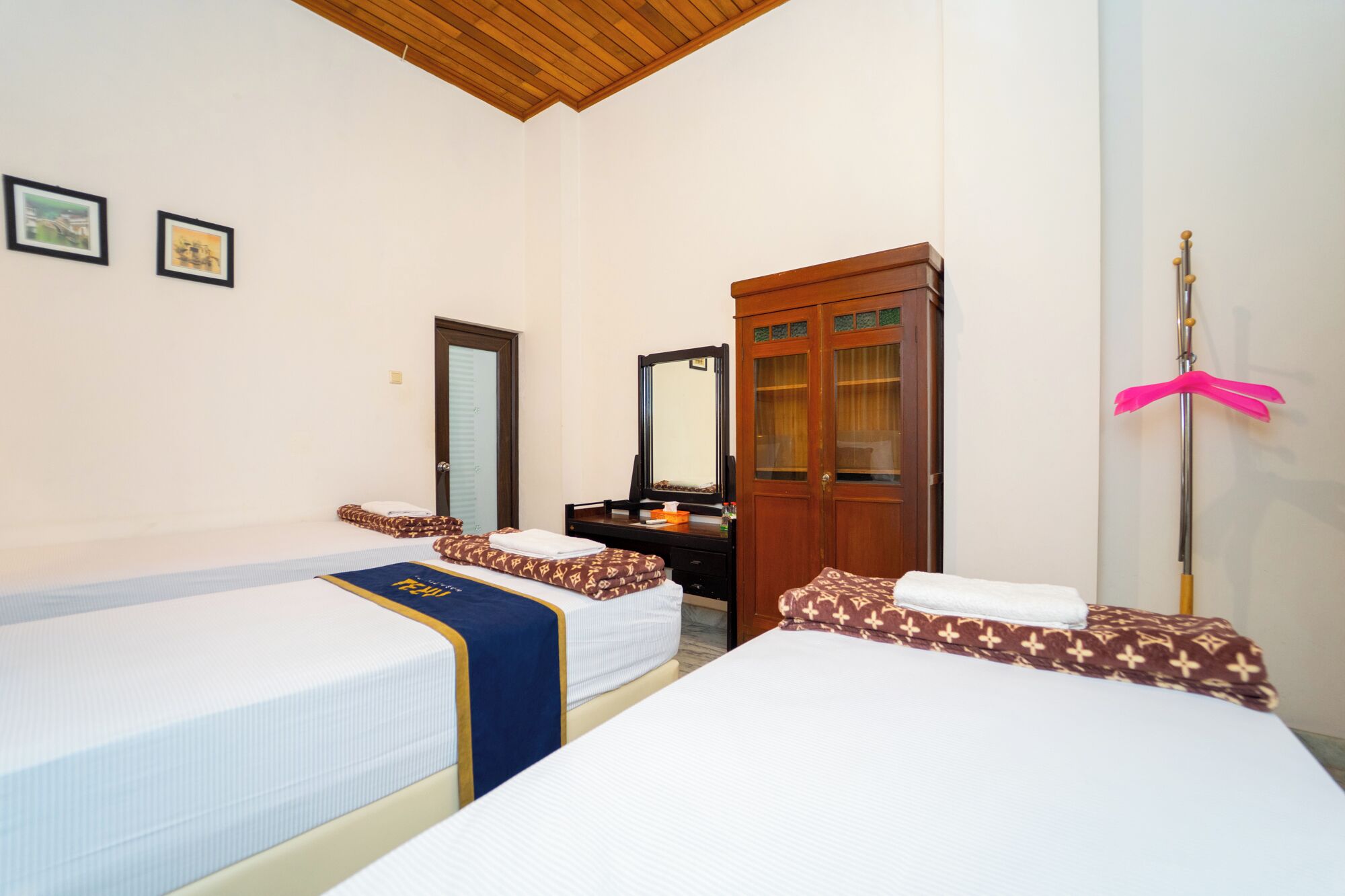 A hotel room with two beds, a wooden wardrobe, a mirror, and a pink cleaning tool.