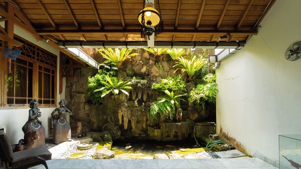 Una habitación con pared de piedra, un pequeño estanque y dos estatuas.