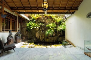 A room with a stone wall, a small pond, and two statues.