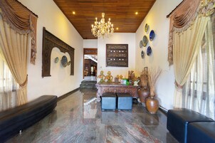 A lobby with a chandelier, ornate wall decorations, a reception desk, and a staircase.