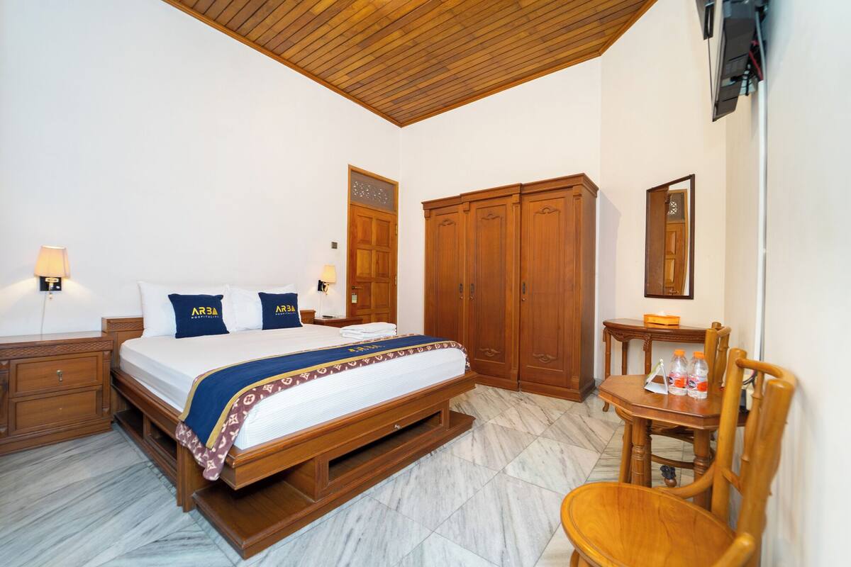 A hotel room with a bed, wooden wardrobe, a small table with chairs, and a mirror.