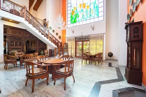 A spacious lobby with a grand staircase, wooden furniture, and a large stained glass window.