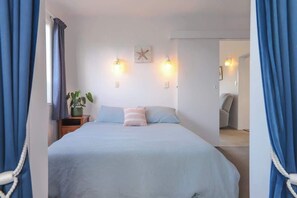 Ein Schlafzimmer mit Bett, Vorhängen, einem Nachttisch mit Pflanze und Wandleuchten.