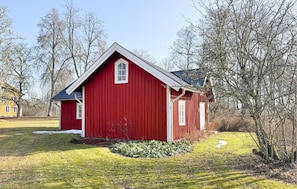 A red wooden house with a gabled roof, surrounded by trees and a grassy yard.