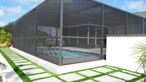 Ein überdachter Swimmingpool mit einer Glasumrandung, umgeben von einer weißen Mauer und einer Rasenfläche.