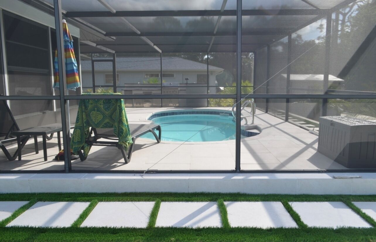 Una piscina exterior techada con un patio, césped y una casa al fondo.