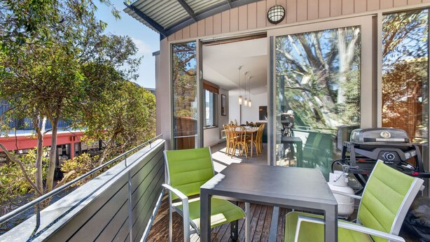 A balcony with a dining table and chairs, a grill, and a view of a red building and trees. - Squatters Run 8: central ski-view stay w/ parking (Thredbo)