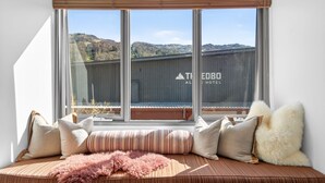 A room with a large window, a cushioned bench, and a view of a hotel building. - Squatters Run 8: central ski-view stay w/ parking (Thredbo)