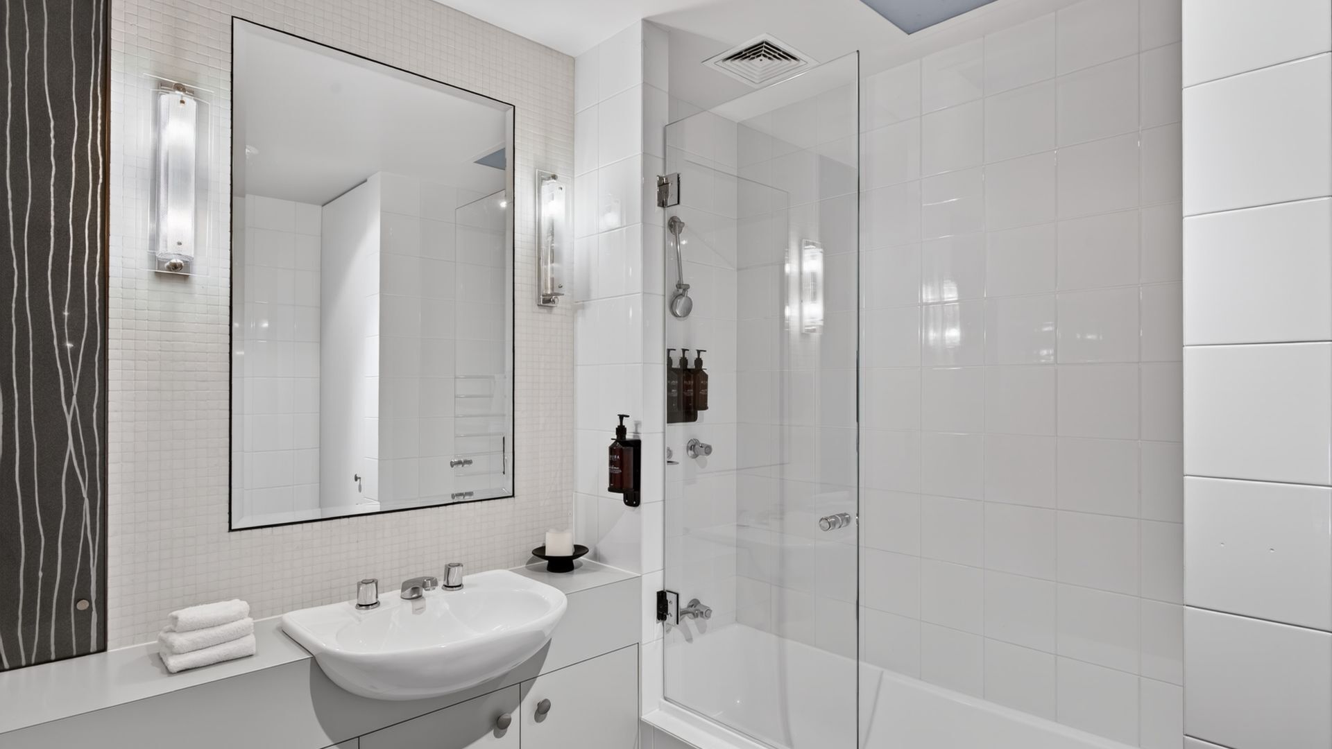A modern bathroom with a large mirror, a sink, and a glass-enclosed shower.
