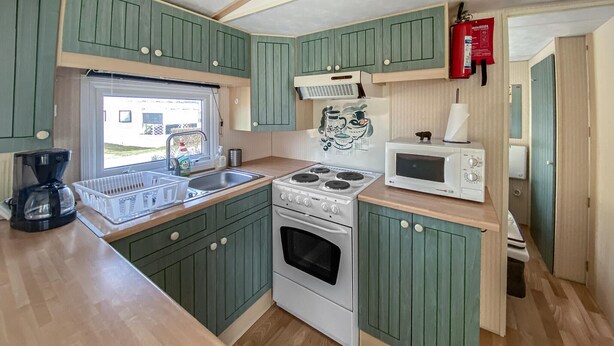 Een kleine keuken met een fornuis, magnetron en spoelbak.