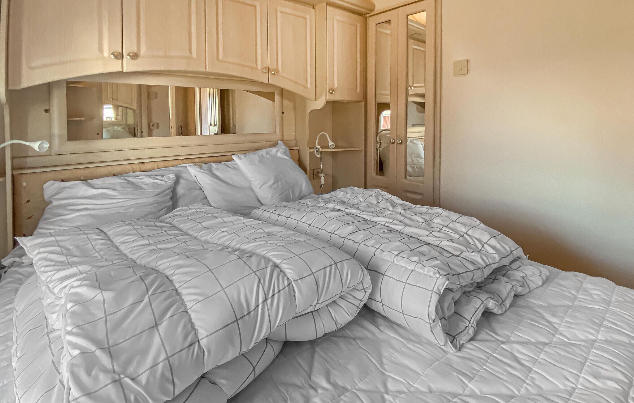 A bed with a quilted cover, a bedside table, a mirror, and a wardrobe with a mirror.
