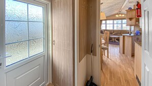 Een gang met een deur van gefroste glas, houten vloeren en een uitzicht op een woonruimte met een bank en een eettafel.