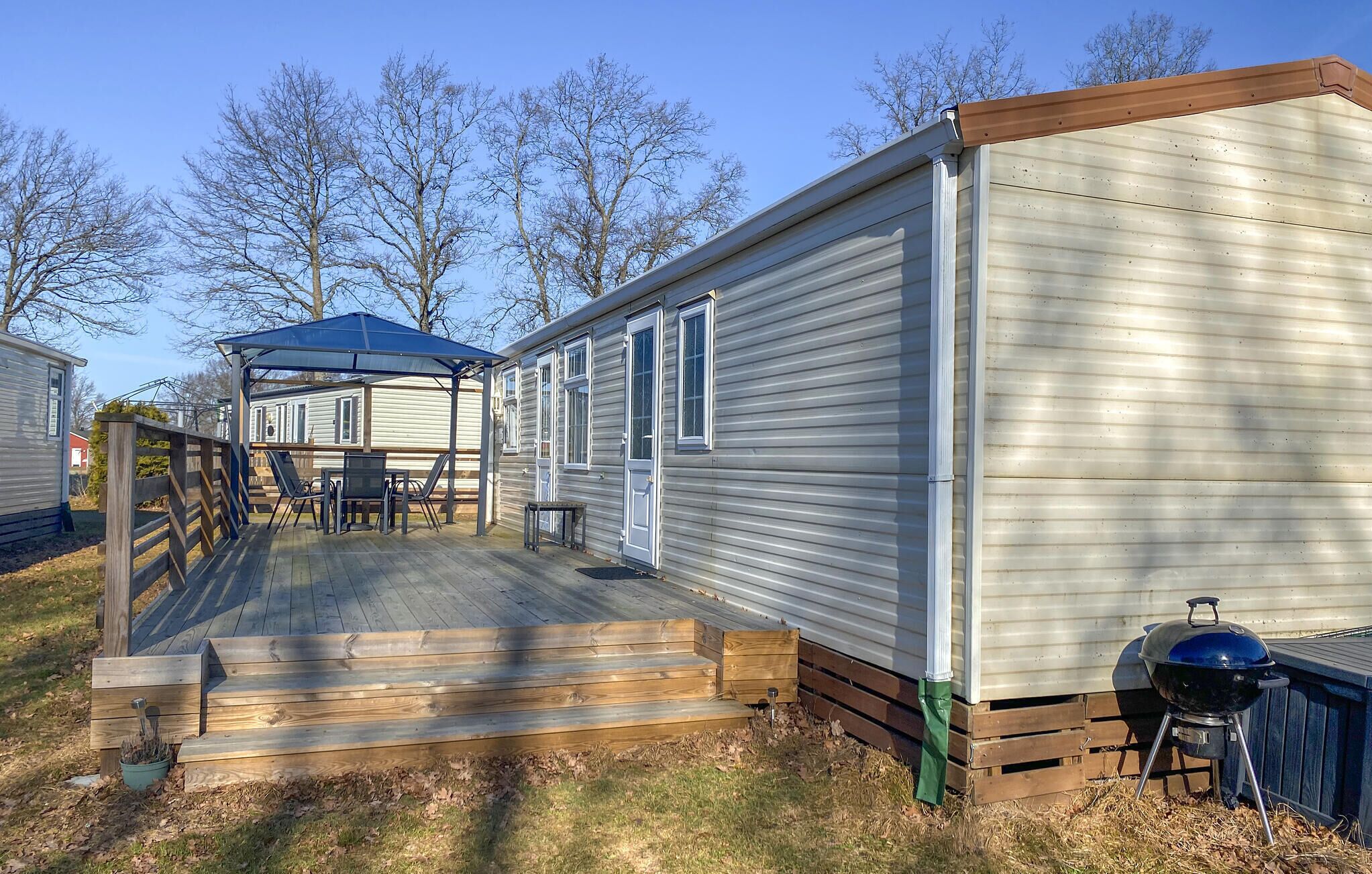 A mobile home with a deck, a barbecue grill, and a covered patio area.