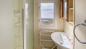 Ein Badezimmer mit weißem Waschbecken, einem Spiegel, einem Fenster und einer Duschkabine.
